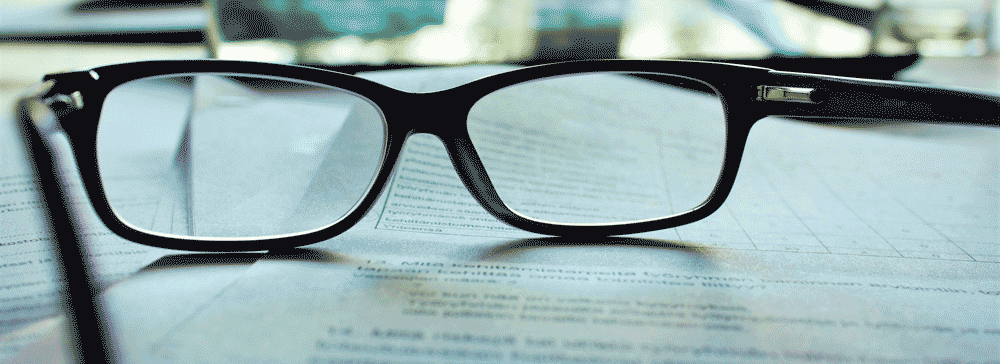 Des lunettes posées sur un document pour évoquer la recherche et la fatigue.